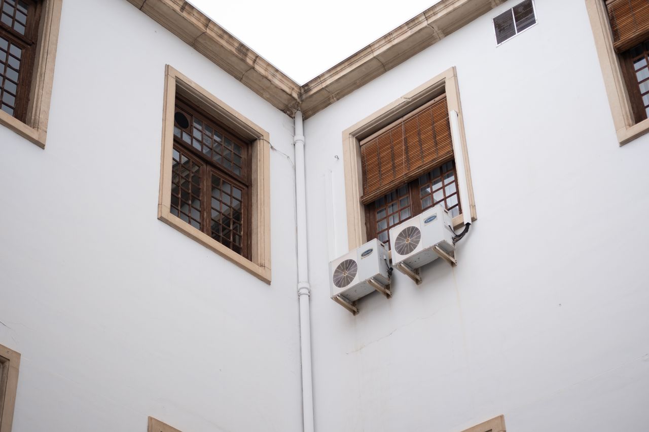 White building facade with wooden window shades and air conditioning units.
